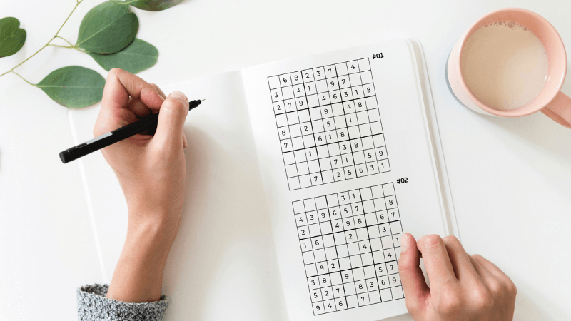 Hands working on a Sudoku puzzle, highlighting the cognitive benefits of puzzles and crosswords for relaxation.